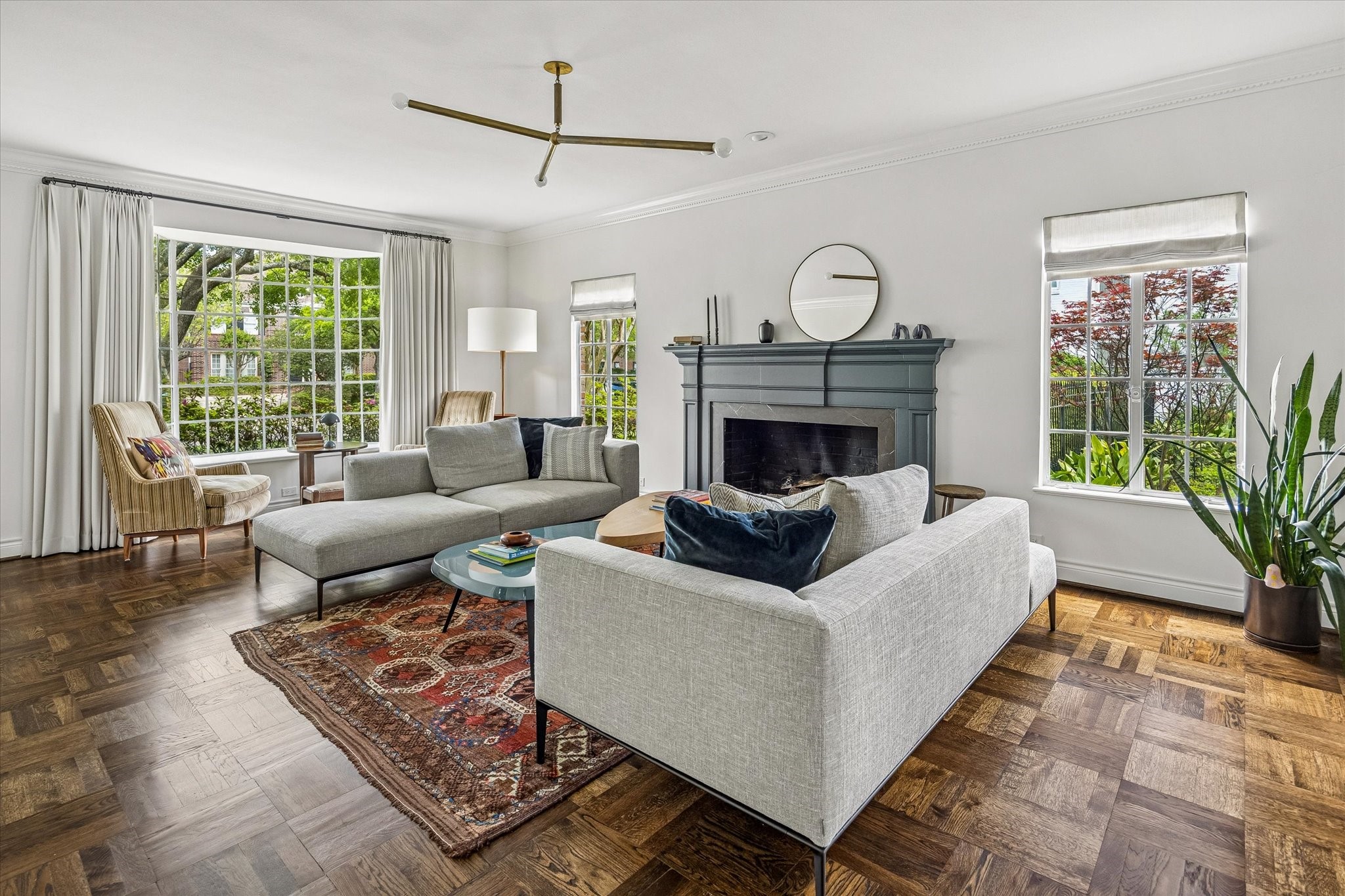 2133 Inwood Drive Houston, TX 77019 - Photo 5 of 22 The living room showcases large windows, continuation of the parquet hardwood floors, and a cozy fireplace, creating a warm, elegant atmosphere.