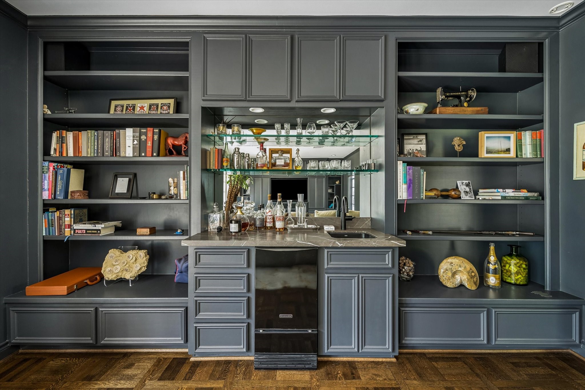 2133 Inwood Drive Houston, TX 77019 - Photo 10 of 22 A custom built-in bar with dark cabinetry and a mirrored backsplash adds a refined focal point to the family room, complemented by shelving for curated display and effortless entertaining.