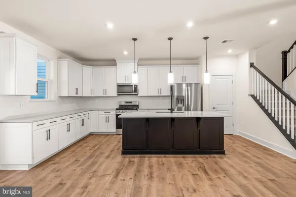 a kitchen with stainless steel appliances granite countertop a sink a stove a refrigerator and white cabinets with wooden floor