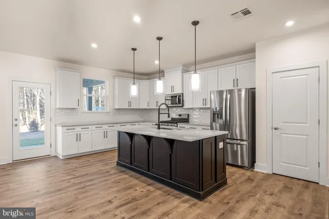 a kitchen with stainless steel appliances granite countertop a sink a oven a refrigerator and white cabinets with wooden floor