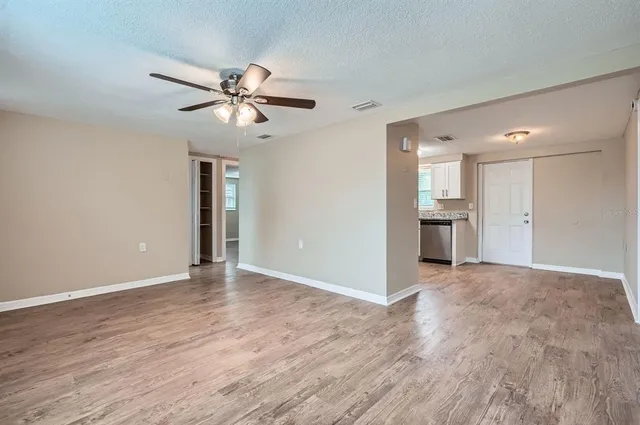 a view of an empty room and kitchen view with wooden floor