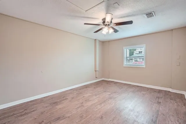 an empty room with wooden floor fan and windows