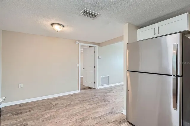 a view of an empty room with wooden floor and a refrigerator