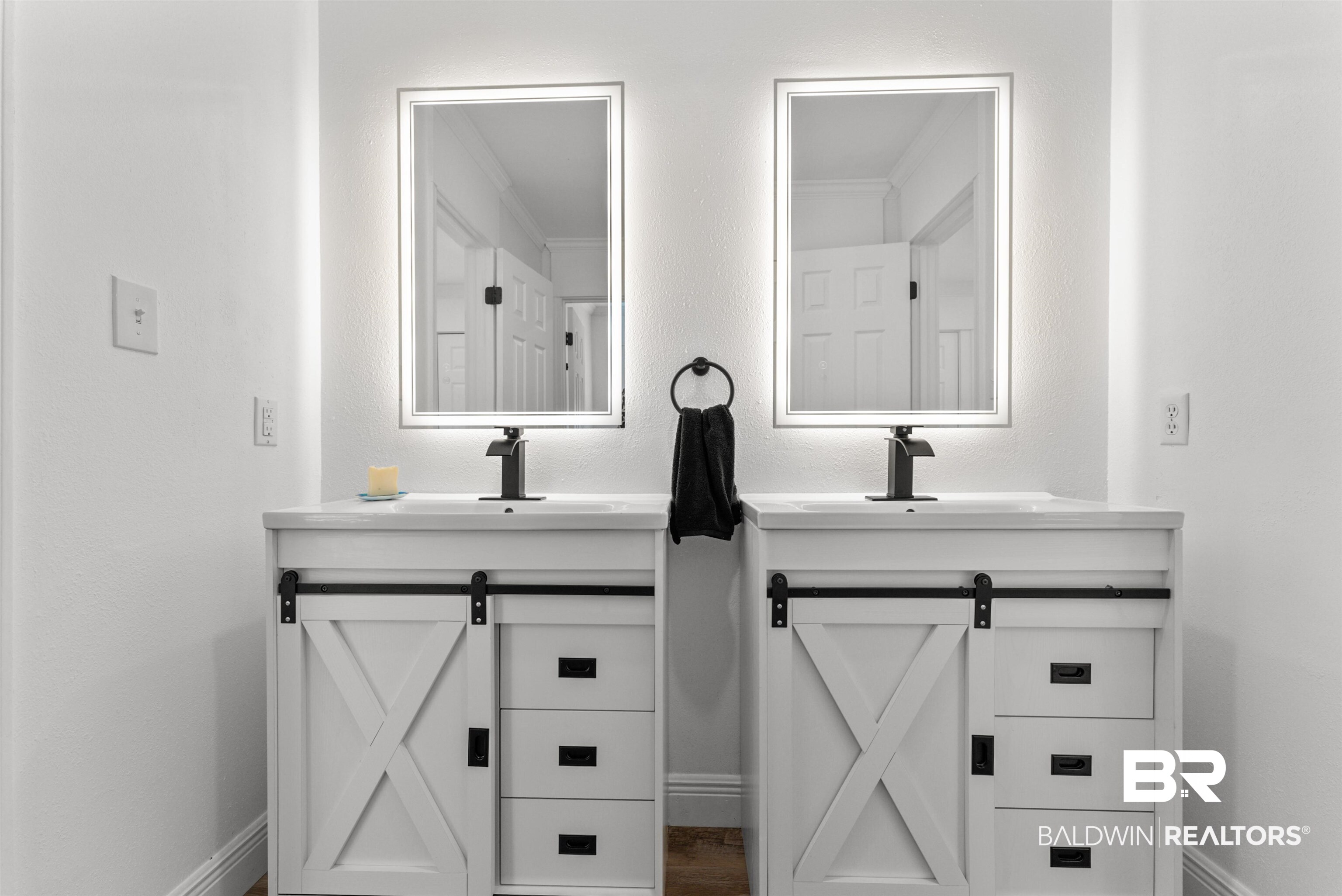 6447 Bemis Lane Bon Secour, AL 36511 - Photo 50 of 62 Dual vanities featuring white shaker-style cabinetry with black barn door hardware, integrated sinks, black faucets, and rectangular backlit mirrors