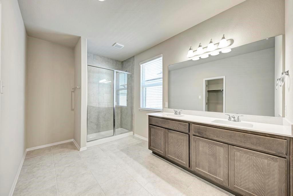 1209 Goforth Road Kyle, TX 78640 - Photo 17 of 32 A well-lit primary bathroom featuring a double vanity, a spacious walk-in shower, and ample natural light.
