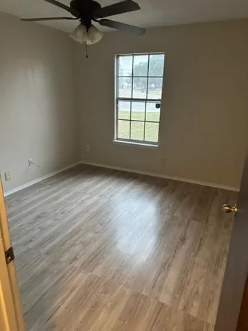 an empty room with wooden floor fan and windows