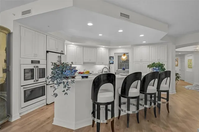 a kitchen with stainless steel appliances kitchen island granite countertop a refrigerator a stove a microwave oven a dining table and chairs with wooden floor