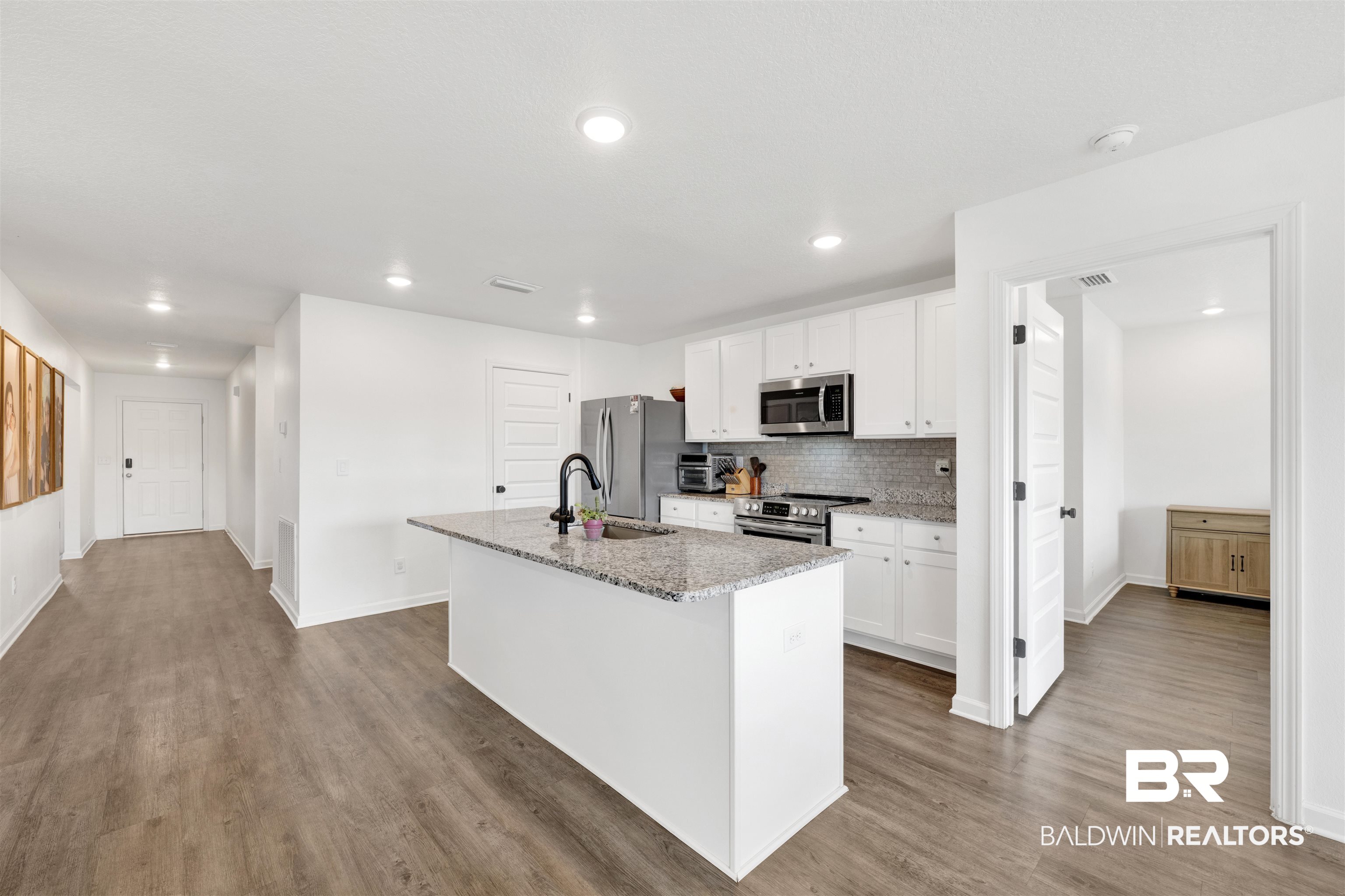 10763 Paget Drive North Mobile, AL 36608 - Photo 4 of 24 Kitchen with white cabinets, an island with sink, dark wood-type flooring, stainless steel appliances, and light stone counters