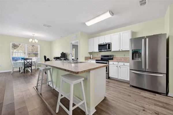 a kitchen with stainless steel appliances a refrigerator a stove a sink a dining table and chairs with wooden floor