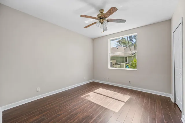an empty room with wooden floor ceiling fan and window
