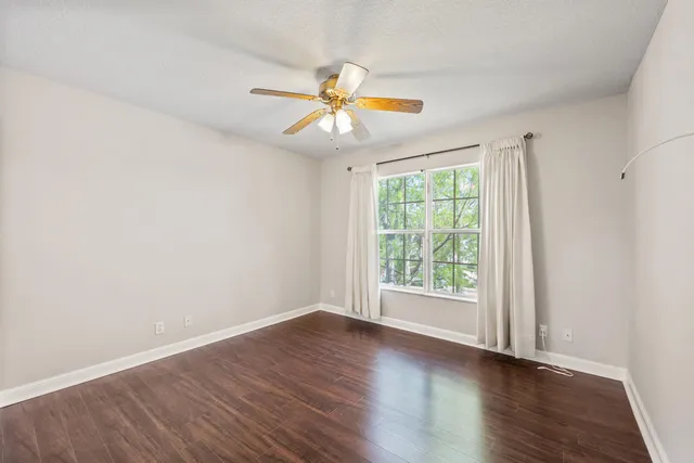 an empty room with wooden floor fan and windows