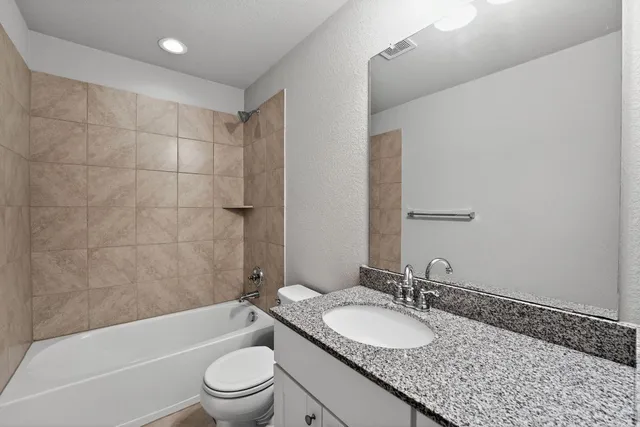 a bathroom with a granite countertop sink a toilet a mirror and bathtub