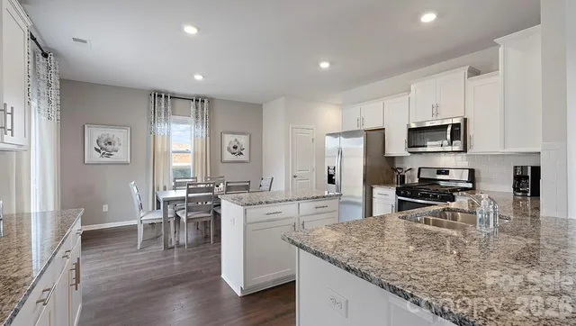 a kitchen with stainless steel appliances granite countertop a stove top oven a sink a dining table and chairs