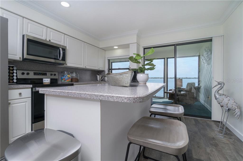 5041 North Beach Road, Unit 3A Englewood, FL 34223 - Photo 16 of 52 a kitchen with stainless steel appliances granite countertop a sink dishwasher stove top oven a dining table and chairs with wooden floor