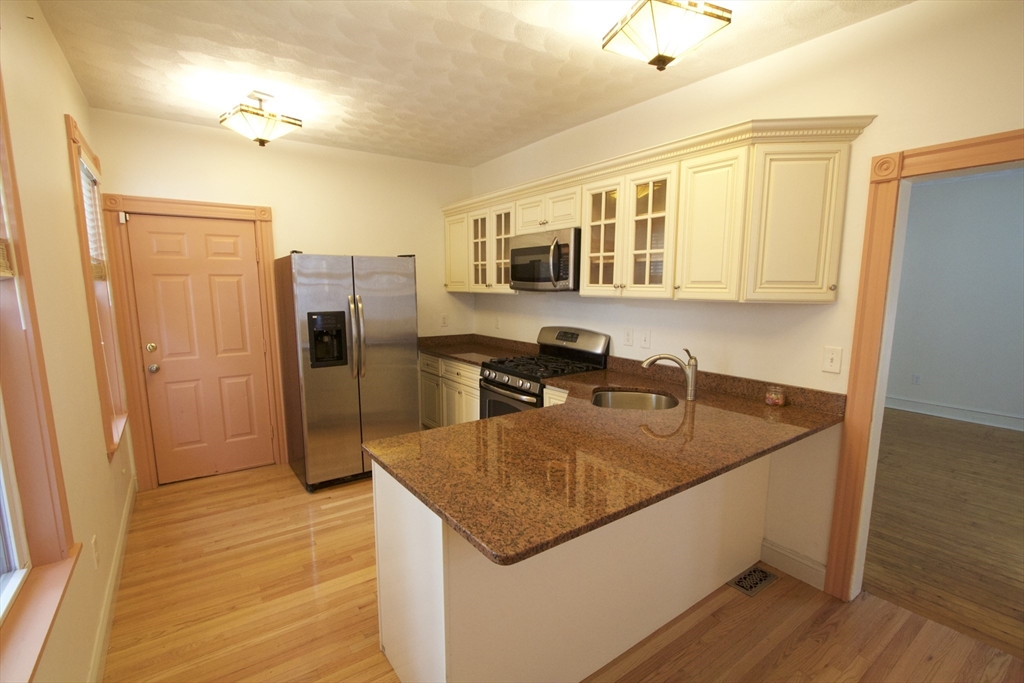 31 Dunreath Street, Unit 1 Boston, MA 02119 - Photo 1 of 11 a kitchen with stainless steel appliances granite countertop a sink a refrigerator and wooden floor