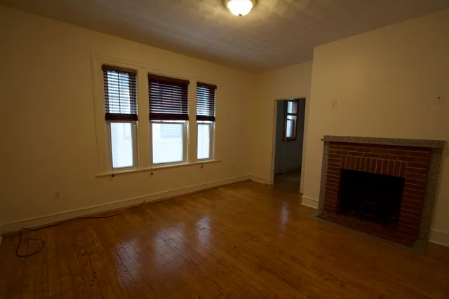a view of an empty room with wooden floor fireplace and a window