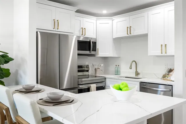 a kitchen with stainless steel appliances a sink a microwave a refrigerator a stove a white table and chairs