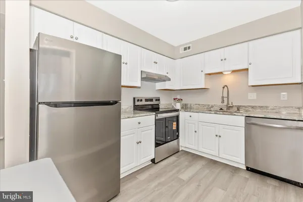 a kitchen with granite countertop a refrigerator a sink and white cabinets
