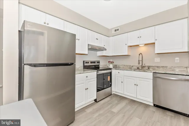 a kitchen with granite countertop a refrigerator a sink and white cabinets