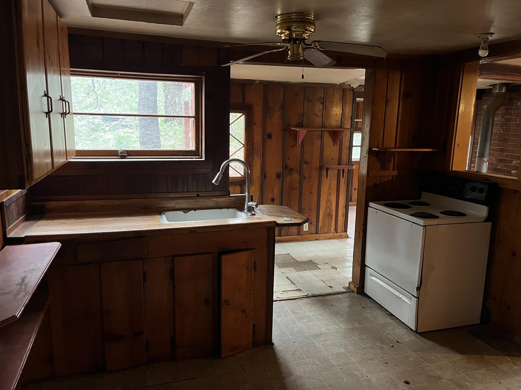 23090 North Bald Mountain Road Sonora, CA 95370 - Photo 40 of 59 Kitchen featuring wooden walls, white range with electric cooktop, a ceiling fan, light floors, and dark wood finish cabinetry