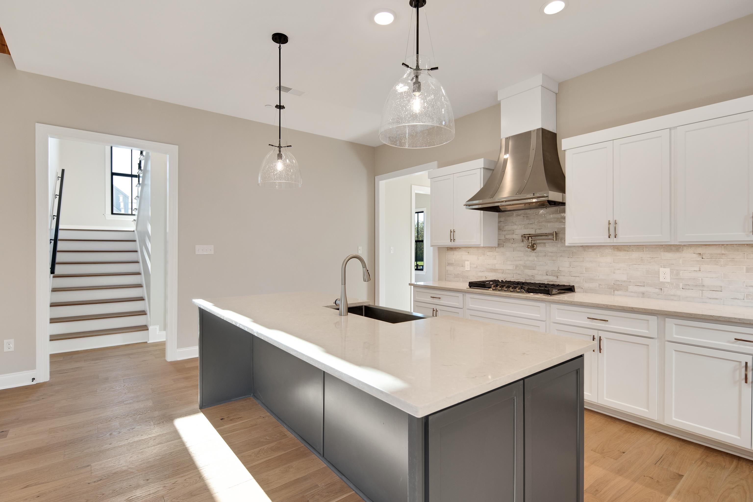 300 Mary Taylor Way Piperton, TN 38017 - Photo 12 of 36 Kitchen featuring sink, wall chimney range hood, stainless steel gas stovetop, a center island with sink, and white cabinets