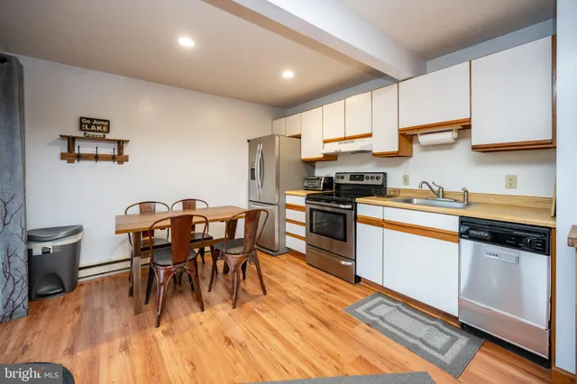 a kitchen with stainless steel appliances granite countertop a stove a refrigerator a sink a dining table and chairs with wooden floor