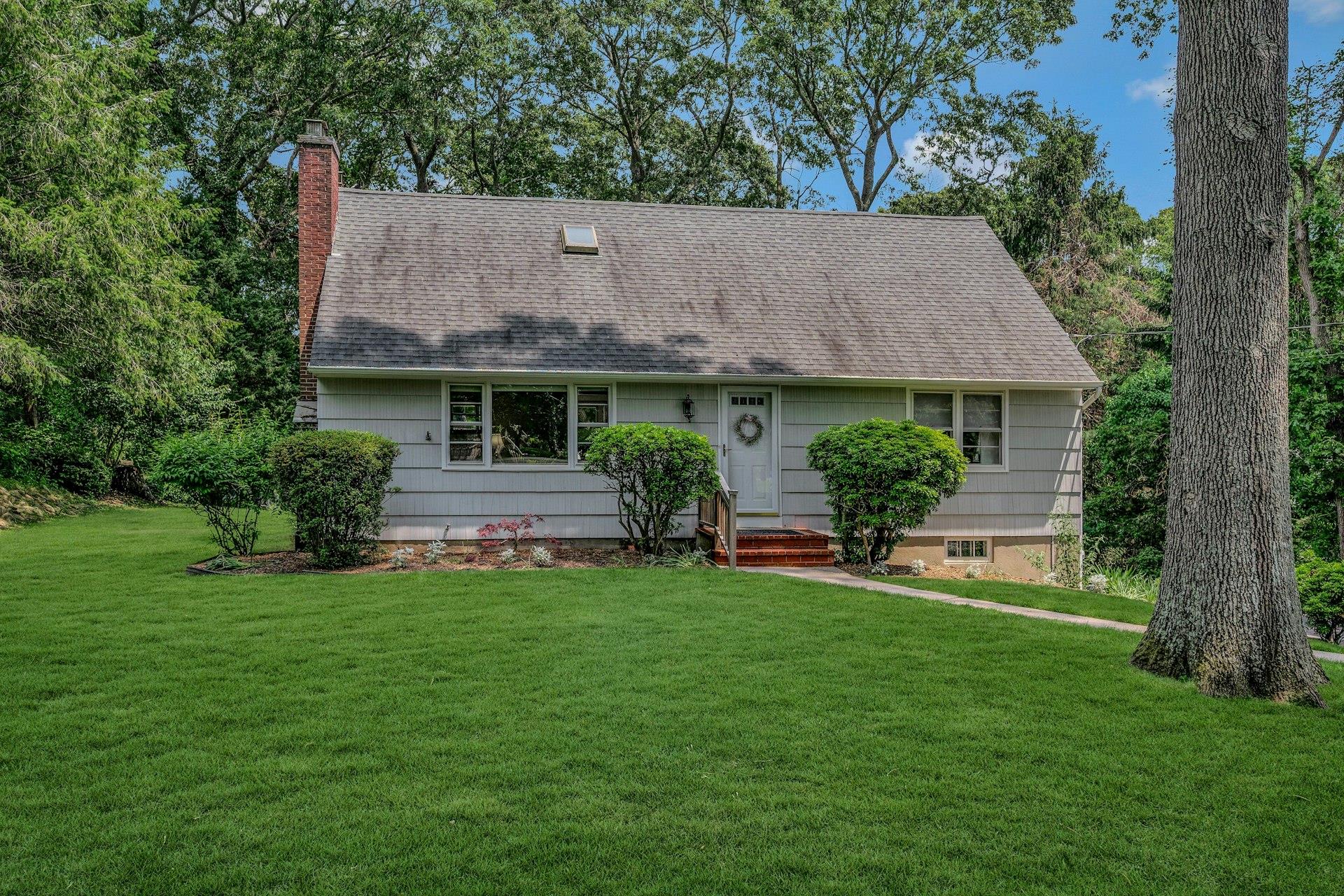 View of front facade with a chimney, a front lawn, and a shingled roof