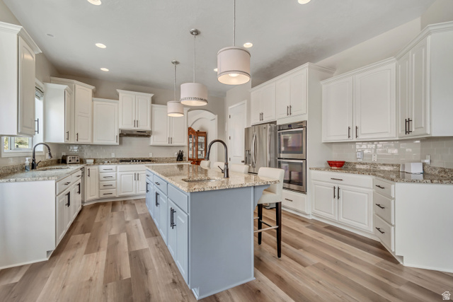 2543 East 700 South Springville, UT 84663 - Photo 28 of 73 Two tone kitchen with decorative backsplash, hanging light fixtures, a kitchen breakfast bar, light stone counters, and light wood-type flooring