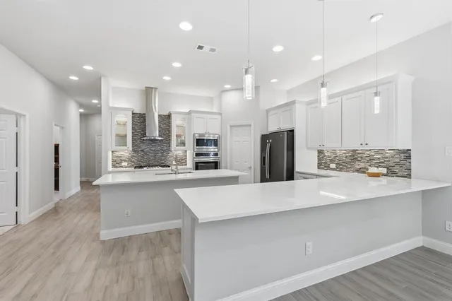 a large kitchen with stainless steel appliances a large counter top a refrigerator and cabinets