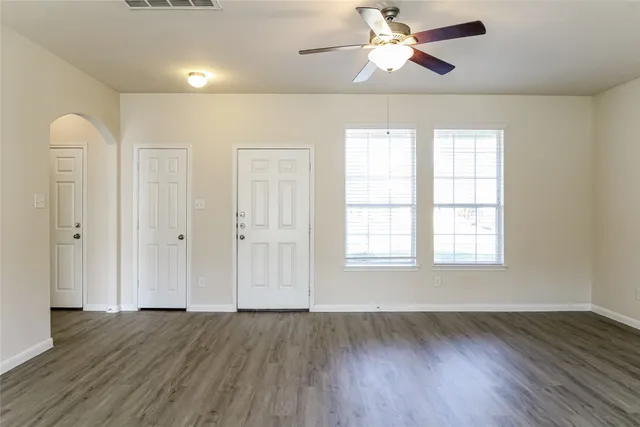 an empty room with wooden floor chandelier fan and windows