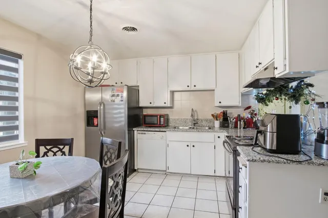 a kitchen with stainless steel appliances granite countertop a sink dishwasher a refrigerator a stove a dining table and chairs with wooden floor