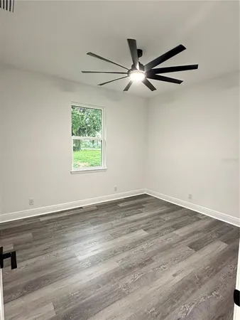 an empty room with wooden floor fan and windows