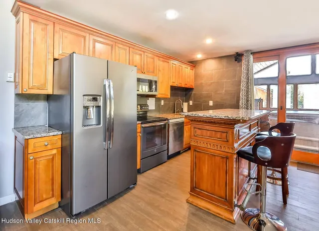 a kitchen with stainless steel appliances a refrigerator a stove a sink dishwasher and chairs with wooden floor