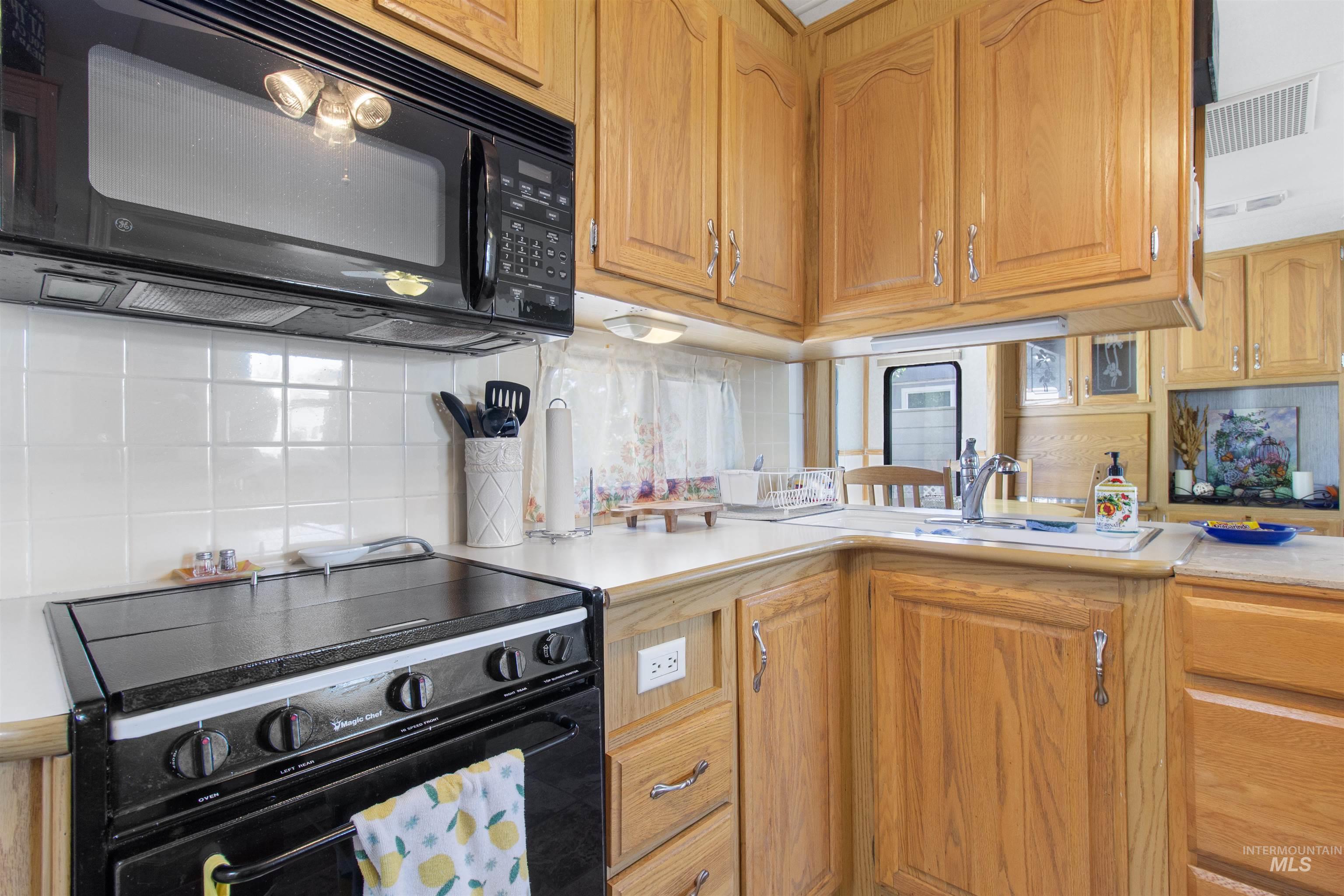106 West Magic Road Shoshone, ID 83352 - Photo 20 of 45 Kitchen featuring light wood cabinetry, white tile backsplash, black overhead microwave, black range oven, and a double basin sink with a chrome faucet