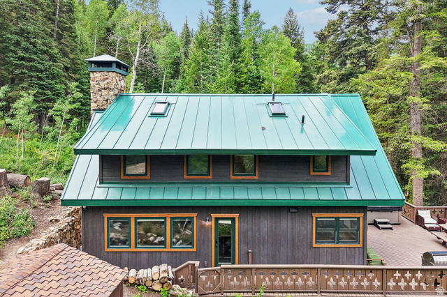 10205 East Moose Loop Road Salt Lake City, UT 84121 - Photo 2 of 50 Mountain-style residence featuring a vibrant green metal roof, stone chimney, and dark wood siding