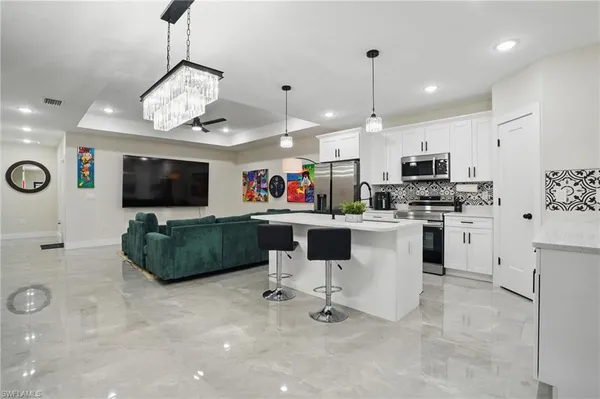 a living room with stainless steel appliances furniture a flat screen tv and kitchen view