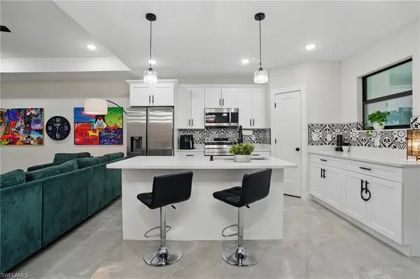 a kitchen with stainless steel appliances kitchen island granite countertop a refrigerator a oven a sink a dining table and chairs with wooden floor