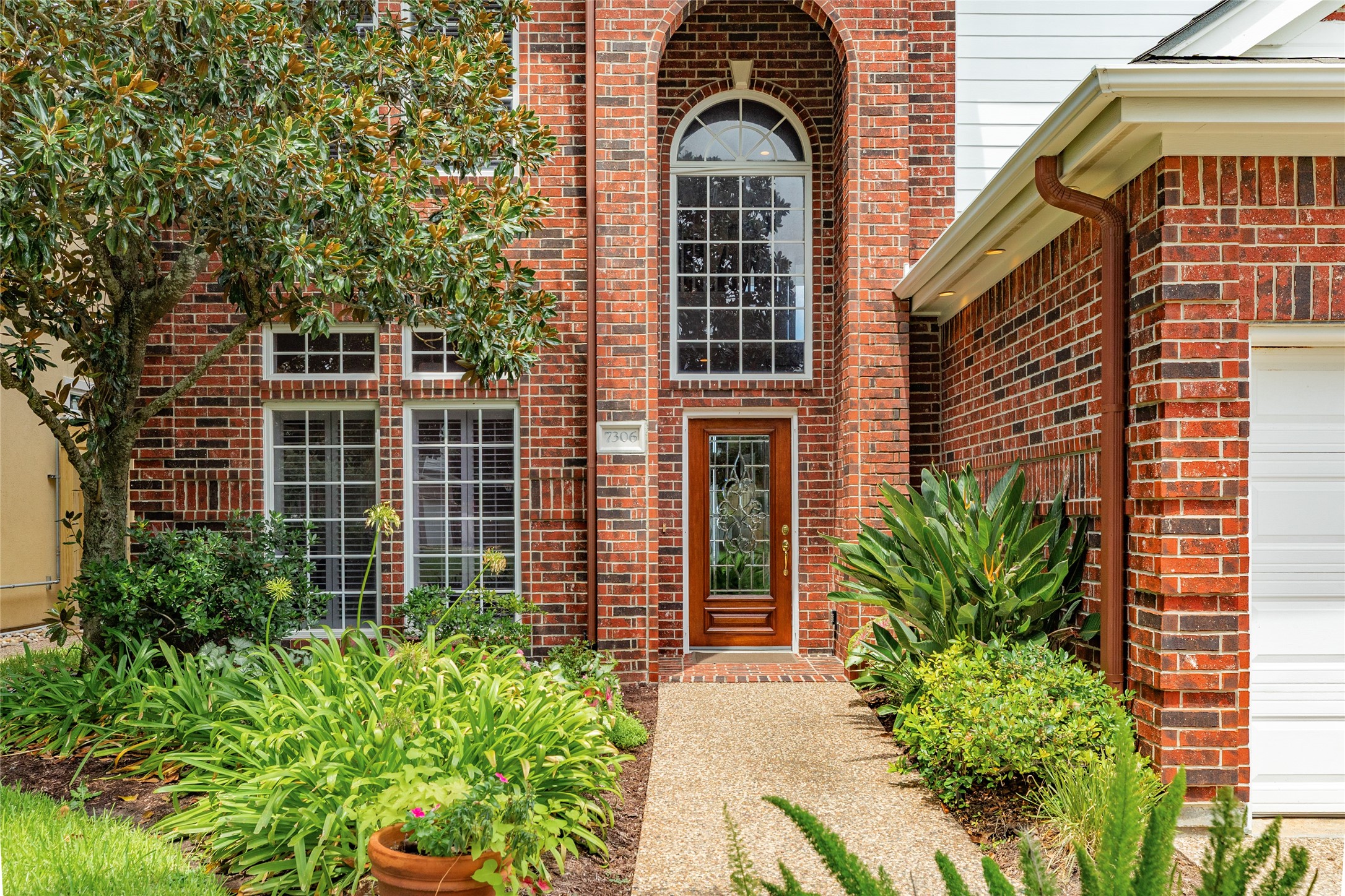 7306 Offats Point Circle Galveston, TX 77551 - Photo 5 of 50 a view of a brick house with plants and a large tree