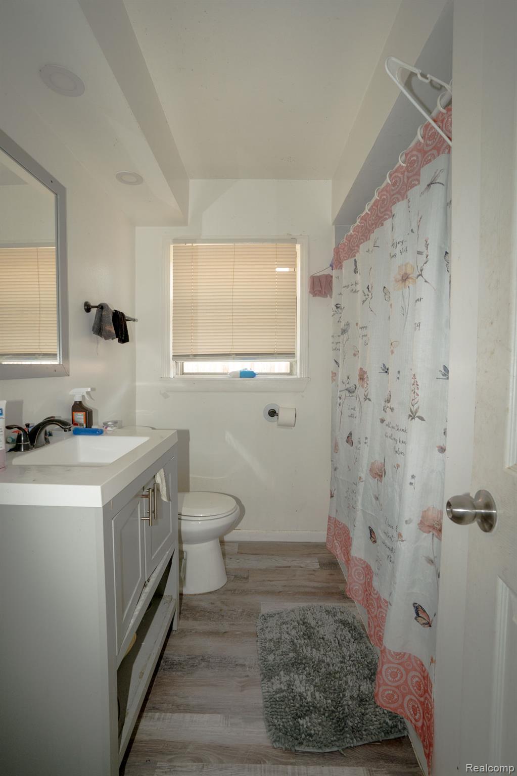 16821 East Eight Mile Road Eastpointe, MI 48021 - Photo 13 of 31 Bathroom featuring a grey vanity with a white countertop and integrated sink, a wall-mounted mirror, a commode, and wood-finish flooring