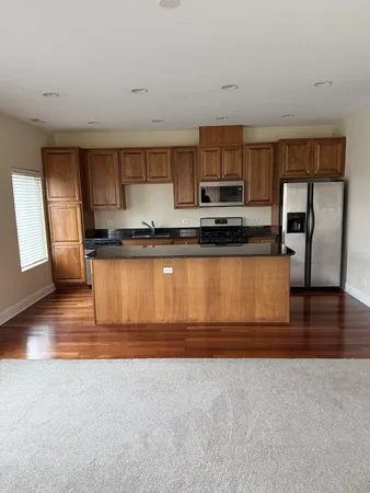 a large kitchen with stainless steel appliances granite countertop a stove a sink a refrigerator white cabinets and a wooden floor