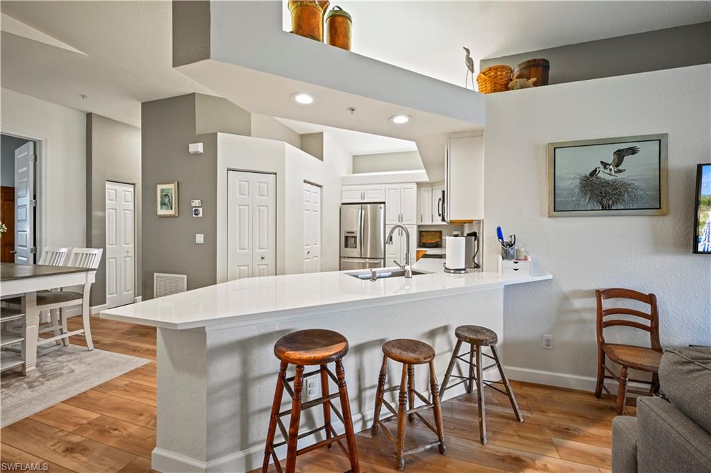 23810 Marbella Bay Road, Unit 203 Estero, FL 34135 - Photo 2 of 47 Kitchen featuring sink, light wood-type flooring, stainless steel fridge, kitchen peninsula, and white cabinets