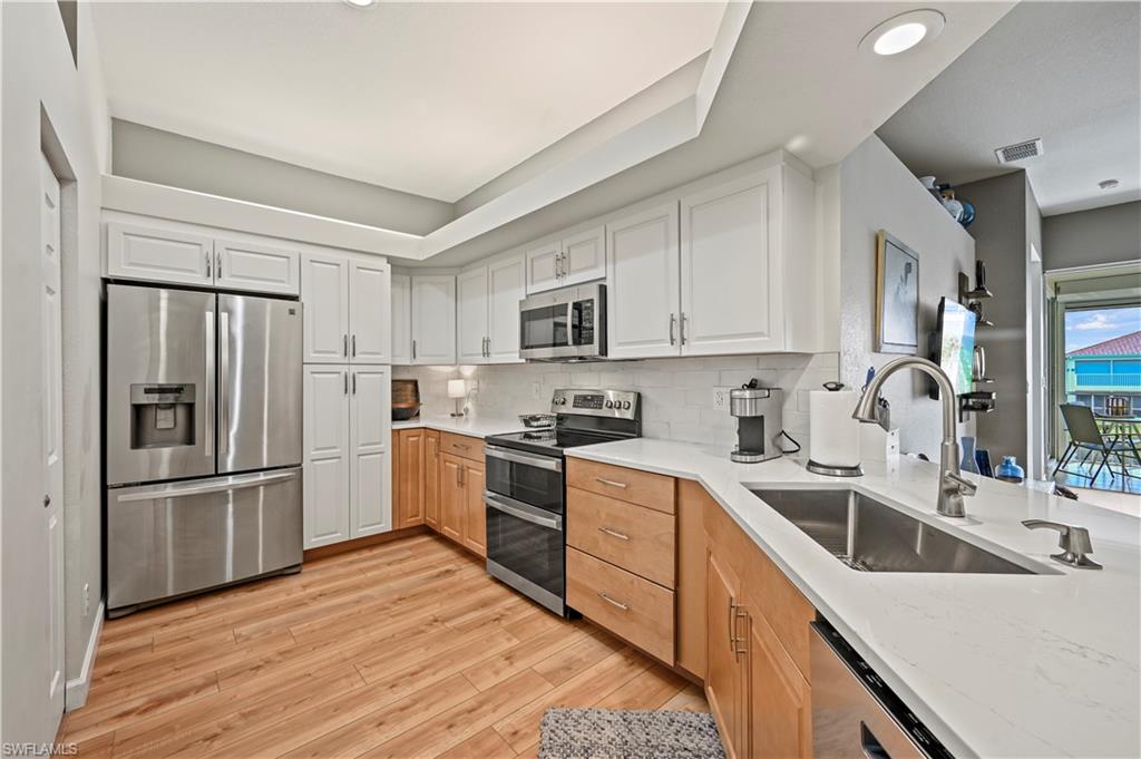23810 Marbella Bay Road, Unit 203 Estero, FL 34135 - Photo 3 of 47 Kitchen with backsplash, sink, light hardwood / wood-style floors, white cabinetry, and stainless steel appliances