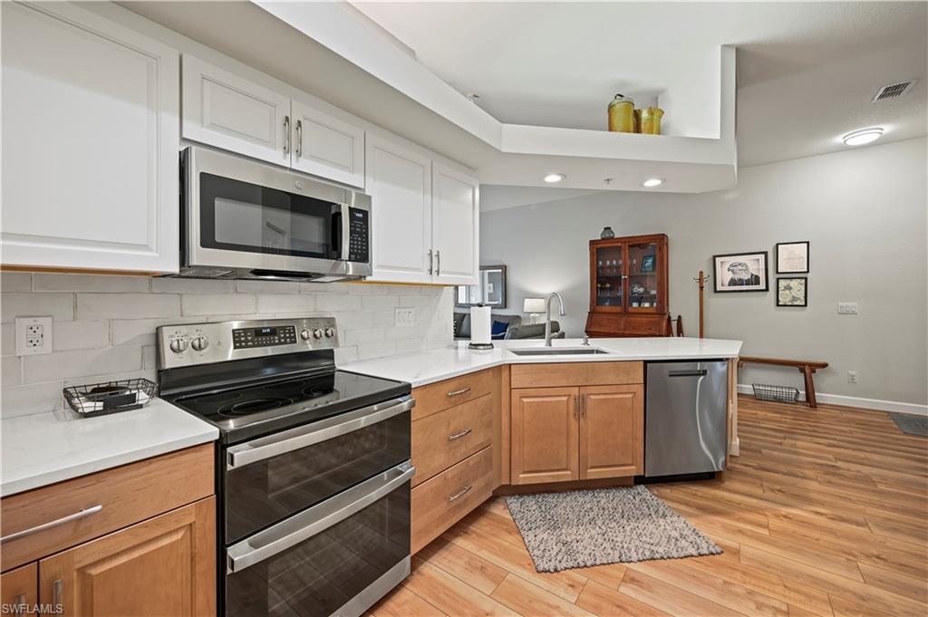23810 Marbella Bay Road, Unit 203 Estero, FL 34135 - Photo 4 of 47 Kitchen featuring backsplash, white cabinetry, light hardwood / wood-style floors, kitchen peninsula, and stainless steel appliances