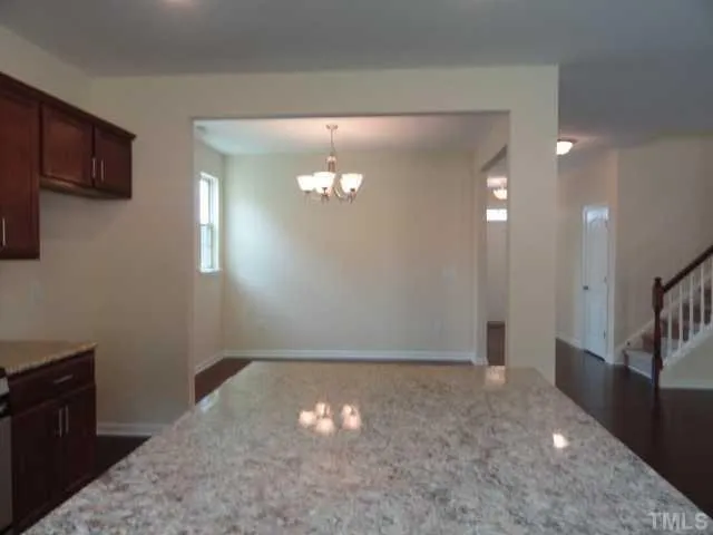 a view of an empty room with wooden floor and a kitchen