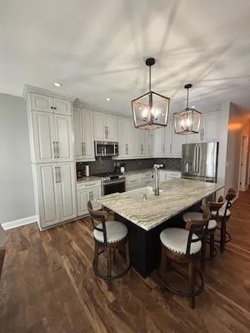 a open kitchen with stainless steel appliances granite countertop a stove a refrigerator a sink a dining table and chairs with wooden floor