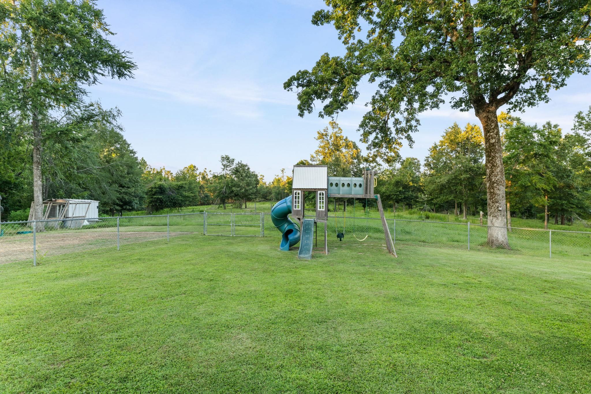 66 County Road 511 Corinth, MS 38834 - Photo 31 of 40 Expansive green lawn with chain link perimeter fencing, featuring mature trees and a built-in play structure with slides and swings