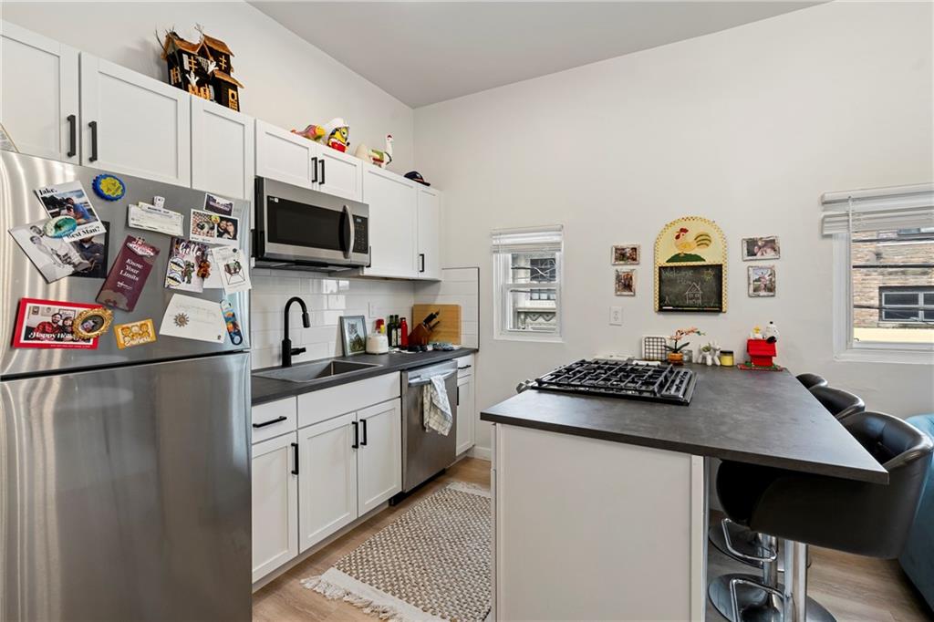 5140 Butler Street Pittsburgh, PA 15201 - Photo 11 of 25 a kitchen with stainless steel appliances granite countertop a stove top oven a sink dishwasher and a refrigerator with wooden floor