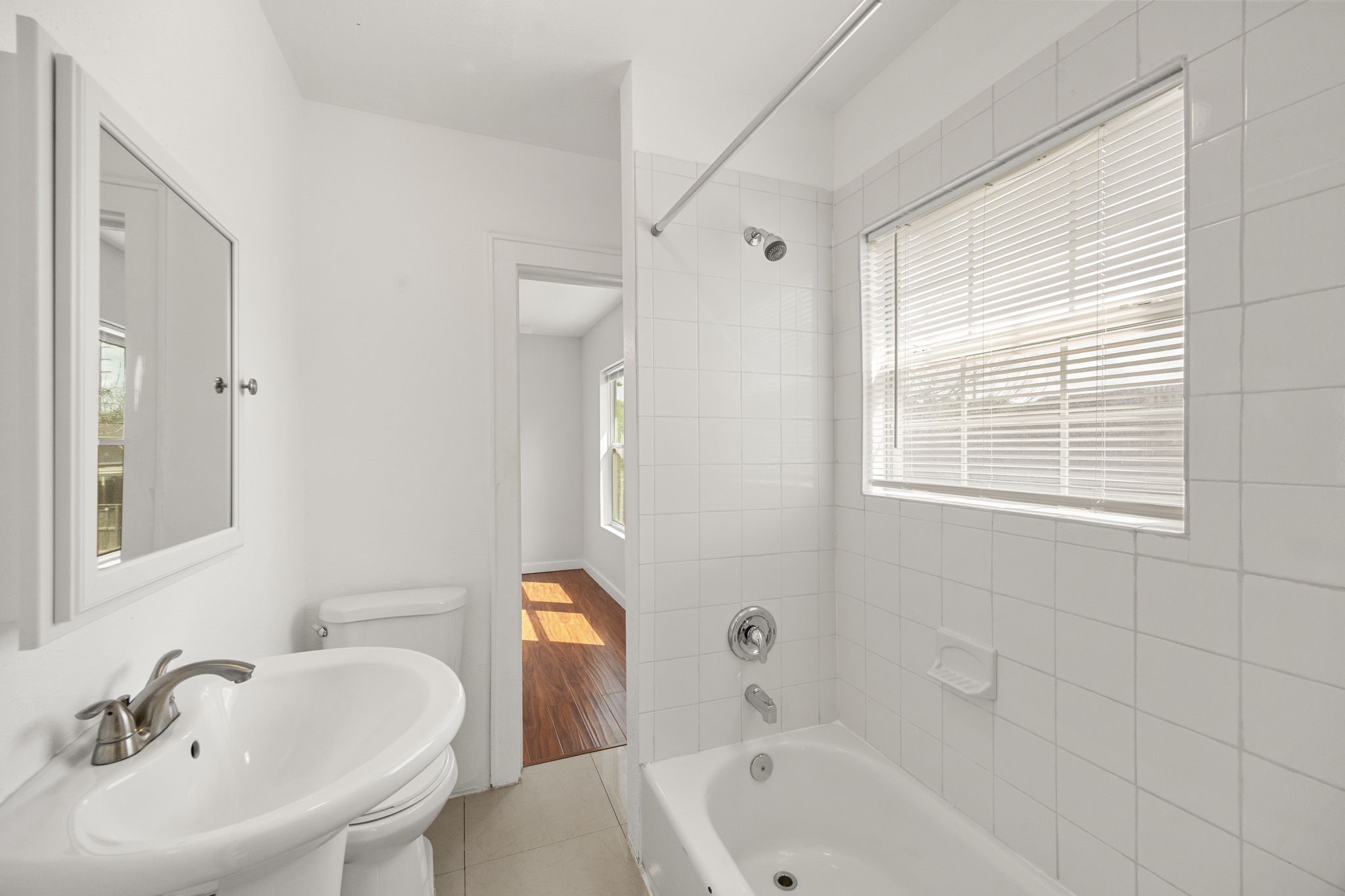 7 Latham Street Houston, TX 77011 - Photo 14 of 23 Clean and functional bathroom featuring a full tub/shower combo, pedestal sink, and natural light from the window.