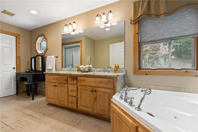 a bathroom with a granite countertop sink a large mirror and a bathtub next to a window