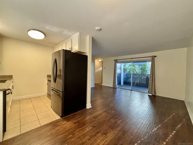 a view of a refrigerator in kitchen and an empty room with wooden floor and a window